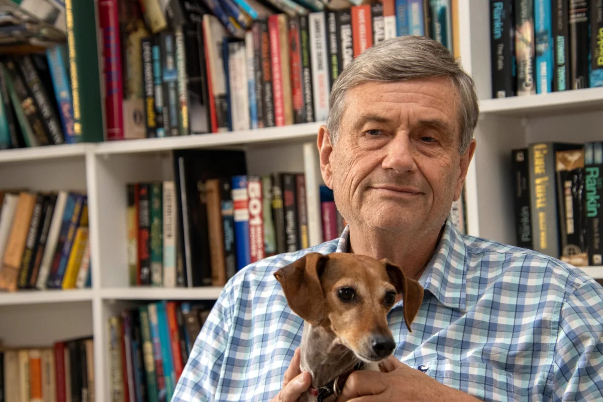 Man holding a small dog in front of bookshelves